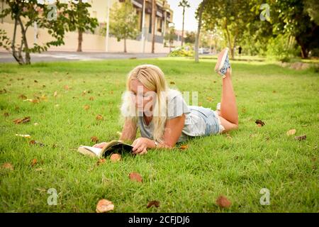 Jeune femme lisant un livre dans un parc, allongé sur l'herbe Banque D'Images