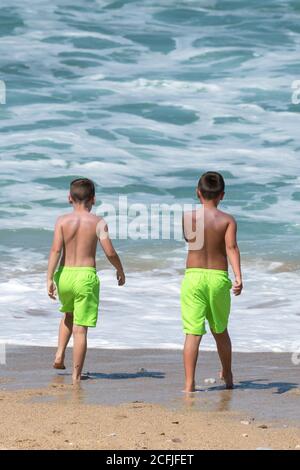 Deux jeunes garçons en vacances de vacances avec des shorts vert lime sur Fistral Beach à Newquay, en Cornouailles. Banque D'Images