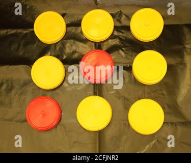 Deux couvercles ronds en plastique rouge et sept couvercles ronds jaunes pour bocaux sur fond noir Banque D'Images