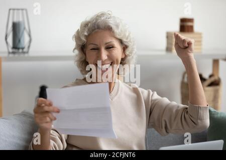 Une femme d'âge moyen souriante et pleine de joie lit les bonnes nouvelles dans la lettre Banque D'Images