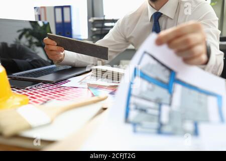 Homme à table tient un projet d'appartement et des échantillons de matériaux de finition. Banque D'Images
