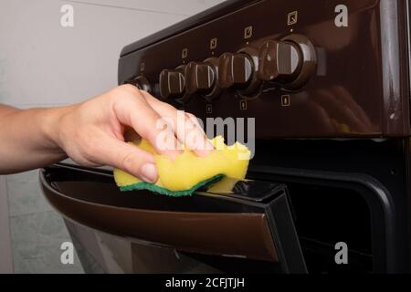 nettoyage de la surface d'un four à gaz à l'aide d'une lavette jaune, nettoyage de la cuisine. Banque D'Images