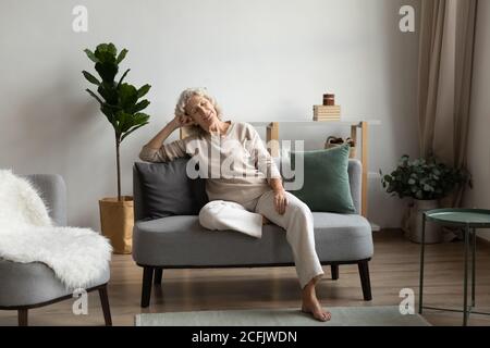 Femme calme et mature assise, reposant sur un canapé confortable à la maison Banque D'Images