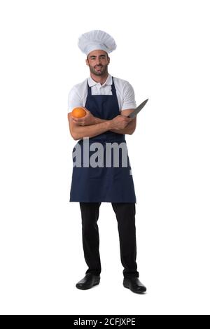 Cuisinier mâle en tablier et chapeau tenant l'orange et le couteau isolé sur fond blanc, portrait pleine longueur Banque D'Images