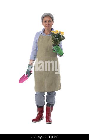 Jardinage. Femme mature jardinier travailleur avec fleurs en pot et pelle isolée sur fond blanc, portrait pleine longueur Banque D'Images