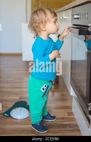 Enfant petit et curieux jouant avec les boutons du four dans la cuisine. Danger pour les enfants sans surveillance, prévention des accidents à la maison phot conceptuel Banque D'Images