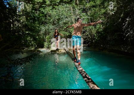 Homme voyageant le long de la bûche et traversant le lac pendant que la femme se fait aider la main et se tient debout sur la rive Banque D'Images