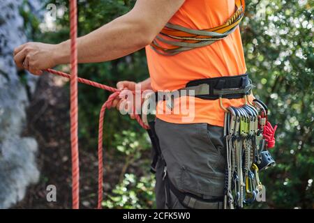 Vue latérale du grimpeur mâle portant la ceinture de sécurité avec mousquetons préparation à l'escalade de la roche en forêt Banque D'Images