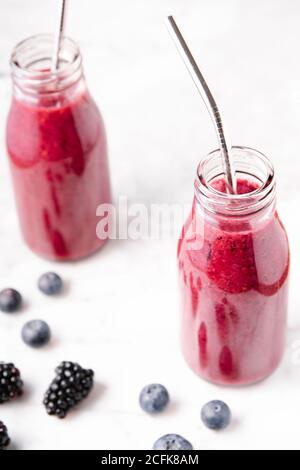 Smoothie aux baies sur des bouteilles en verre sur une surface en marbre blanc. Image verticale à angle élevé. Banque D'Images