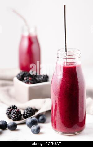 Une bouteille de verre contenant du smoothie aux baies maison rose, avec une paille de métal pour la boire. Image verticale. Banque D'Images