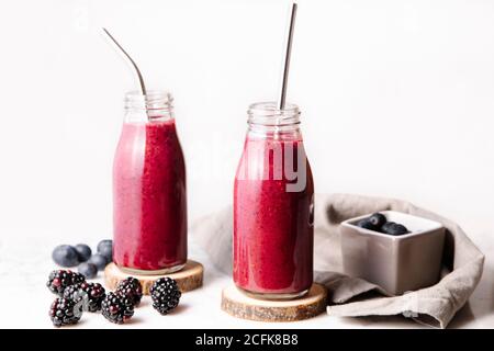 Smoothie aux baies en bouteilles de verre avec pailles métalliques réutilisables. Vue avant avec fond blanc. Banque D'Images