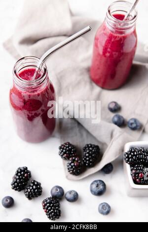 Bouteilles en verre avec smoothies aux baies et pailles en métal. Quelques baies sur une surface en marbre. Banque D'Images
