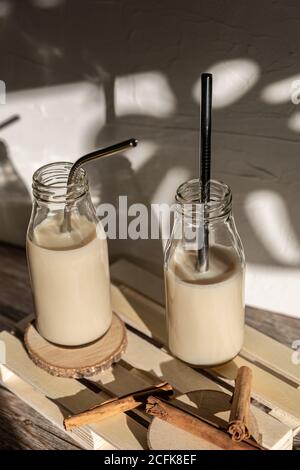 Bouteilles en verre remplies de milk-shake sucré maison et sain à la cannelle placé sur une table en bois contre le mur avec l'ombre de la monstère feuilles Banque D'Images