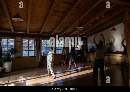 Vue latérale du corps entier d'un instructeur masculin méconnaissable qui fait du chi mouvement de kung ou qigong avec les bras levés pendant la pratique avec étudiants Banque D'Images