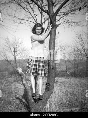 Jeune adolescent des années 1940, qui pose dans un arbre, États-Unis Banque D'Images