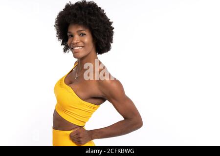 Femme noire dans des vêtements de sport jaunes posant et regardant contre arrière-plan gris Banque D'Images