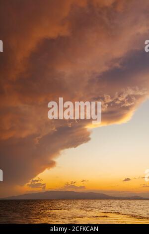 Scène de coucher de soleil derrière les nuages brillants au-dessus de la mer calme et de l'horizon en été. Reflet orange de la lumière du soleil sur les vagues calmes. Le ciel nuageux orange et la mer Méditerranée. Banque D'Images