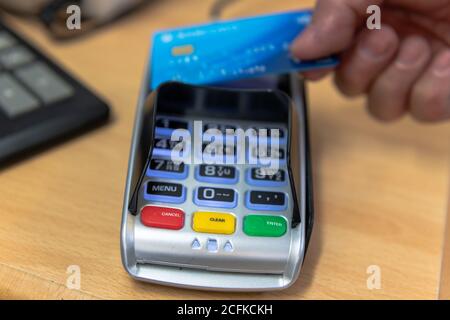 Un client effectuant un paiement par carte sans contact sur un lecteur de carte dans un magasin de détail. Banque D'Images