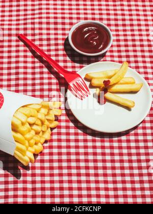 Du dessus des frites paquet près de l'assiette avec les pommes de terre trempées dans le ketchup Banque D'Images