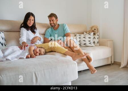 Petite fille dormant sur le canapé pendant qu'un couple enceinte prend soin d'elle à la maison Banque D'Images