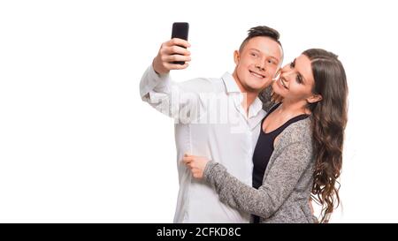 Un jeune couple se serre et sourire tout en faisant du selfie, debout sur un fond blanc isolé. Concept de relations. Banque D'Images