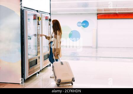une femme avec un masque utilise le distributeur automatique pour acheter une collation Banque D'Images