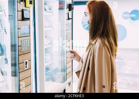 femme avec un masque de visage utilise sa carte de crédit à payez au distributeur automatique Banque D'Images