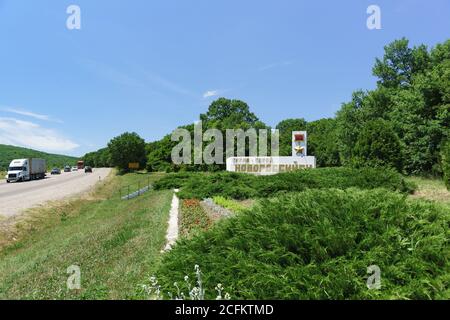 Russie, région de Krasnodar, autoroute fédérale A146 'Krasnodar - Verkhnebakansky' - 12 juin 2018: Stèle à la route avec la circulation dense entourée de vert Banque D'Images