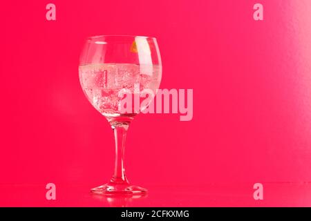 Verre transparent de délicieux gin tonique cocktail avec glace zeste de citron sur la table sur fond rose Banque D'Images