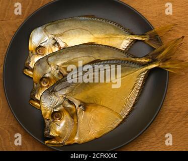 Trois poissons fumés, se trouvent sur une assiette noire, sur une planche en bois Banque D'Images