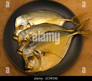 Trois poissons fumés, se trouvent sur une assiette noire, sur une planche en bois Banque D'Images