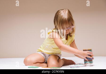 Adorable jeune fille d'âge préscolaire dans des lunettes assises sur le sol et jouant avec des blocs éducatifs colorés Banque D'Images