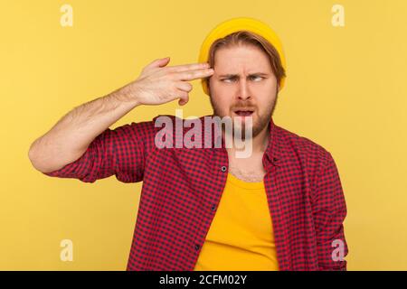 Un gars de taille basse dans un bonnet beanie et une chemise à carreaux se suicider avec un geste de doigt, regardant le cross-eyed drôle d'expression, se sentant fou Banque D'Images