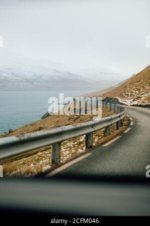 Winding road near river on background of mountain range covered with snow in winter on Faroe Islands Banque D'Images