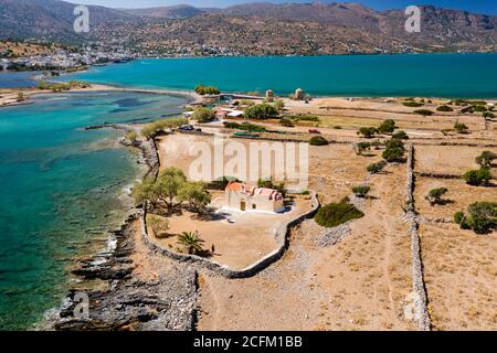Vue aérienne d'une petite église à côté d'un océan bleu sur une île grecque chaude (Eglise de l'Ascension, Elounda, Crète) Banque D'Images