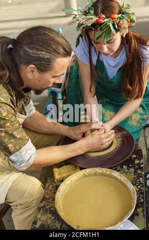 Moldavian, Krymsk, Russie-05 octobre 2019: Un potier enseigne à une fille avec une couronne de fleurs pour faire un pichet d'argile. Master class au festival de Banque D'Images