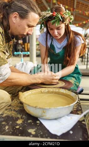 Moldavian, Krymsk, Russie-05 octobre 2019: Un potier enseigne à une fille dans une couronne de fleurs de faire un pichet d'argile. Master class au festival de youn Banque D'Images