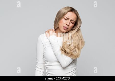 Gros plan portrait en studio d'une jeune femme blonde avec douleur dans le cou et le dos. Arthrite cervicale, ostéochondrose Banque D'Images