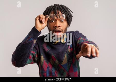 Gros plan surpris Africain choqué avec des dreadlocks mettant hors des lunettes regardant avec les grands yeux et le doigt pointant vers l'appareil photo, vous soupçonnant. Intérieur Banque D'Images