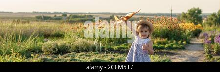 enfance, provence style concept - bannière 3 ans blonde petite fille enfant en robe bleue et chapeau de paille aspect slave courir le long du chemin avec le jouet Banque D'Images