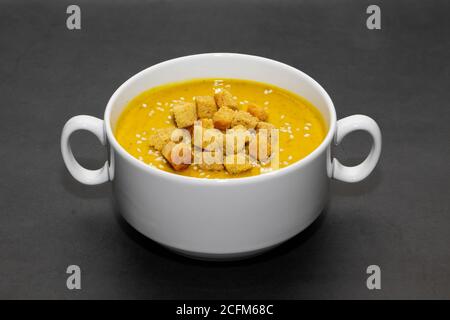 Soupe de crème de citrouille avec craquelins sur fond sombre. Soupe à la crème de citrouille avec craquelins et graines de sésame dans un bouillon blanc sur fond sombre Banque D'Images