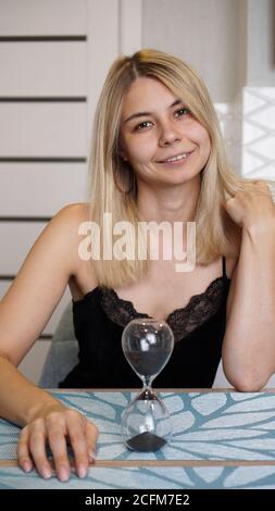 Femme regarde les campeurs et les sourires, concept de temps. Elle est dans une cuisine lumineuse et attend. HourGlass sur la table Banque D'Images