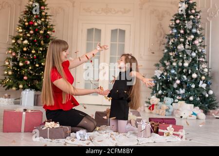 Petite fille avec maa jette confetti et ouvre des cadeaux. Magie de Noël. Des moments joyeux d'une enfance heureuse. Banque D'Images