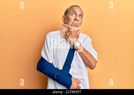 Beau homme mature et âgé portant un col et un bras cervicaux sur une élingue pensant inquiet à une question, inquiet et nerveux avec la main sur le menton Banque D'Images