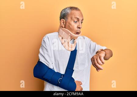 Beau homme mature senior portant col cervical et bras sur le harnais regardant l'heure de la montre inquiet, peur d'être en retard Banque D'Images