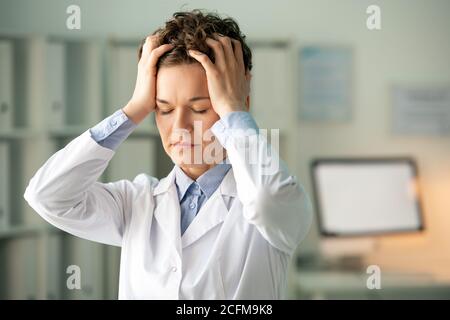 Jeune femme fatiguée chimiste ou pharmacien en blancoat la touchant tête Banque D'Images
