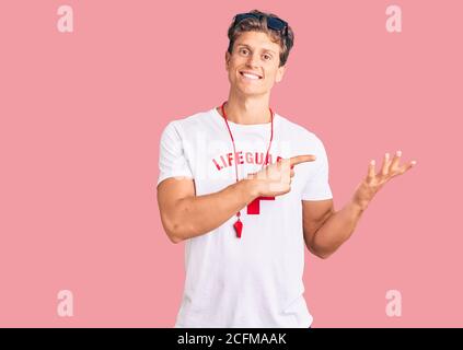 Jeune homme beau portant le t-shirt de maître-nageur et siffler émerveillé et souriant à la caméra tout en présentant avec la main et pointant avec le doigt. Banque D'Images