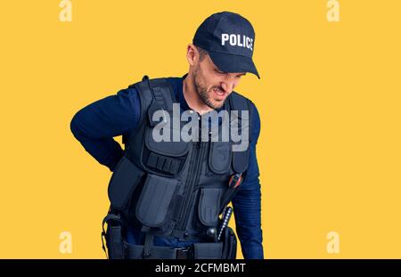 Jeune homme beau portant l'uniforme de police souffrant de mal de dos, se touchant le dos avec la main, douleur musculaire Banque D'Images