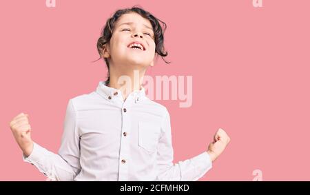 Mignon enfant hispanique portant des vêtements décontractés très heureux et excités faisant le geste gagnant avec les bras levés, souriant et criant pour le succès. Celebratio Banque D'Images
