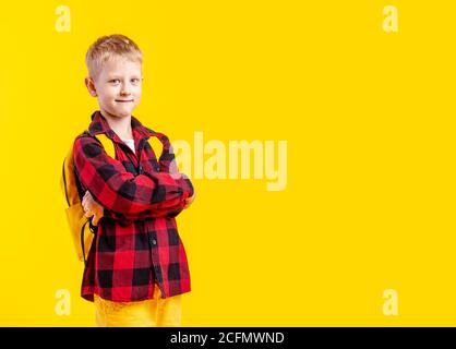 Photo en studio d'un petit écolier confiant avec ses bras croisés sur fond jaune Banque D'Images